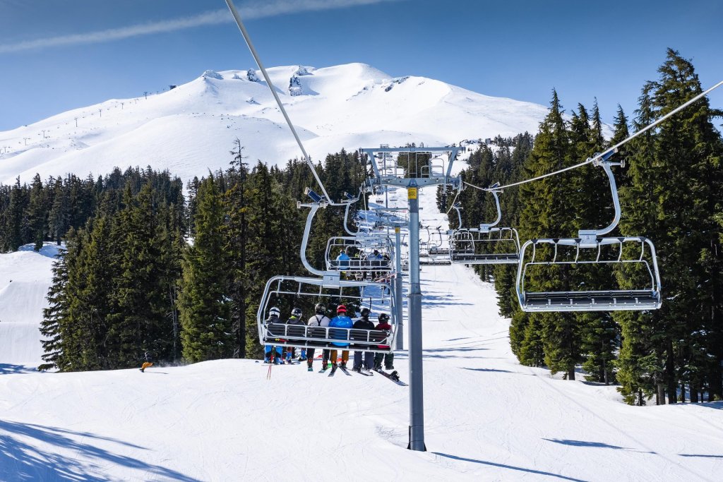 A ski lift carrying skiers up a snowy mountain, surrounded by evergreen trees in Central Oregon.
