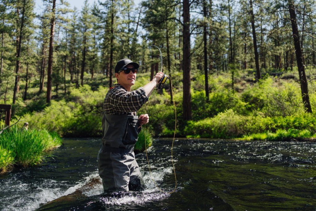 A man fishing in a forest stream, wearing a hat and sunglasses in Central Oregon.