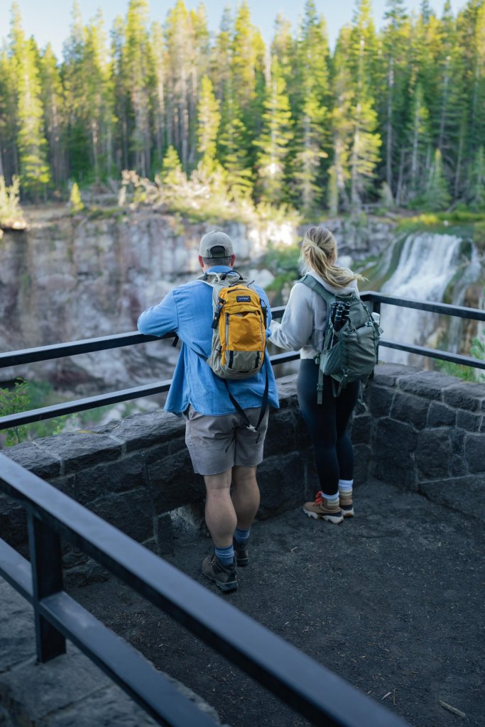Two hikers admire a waterfall from a stone lookout in Central Oregon.