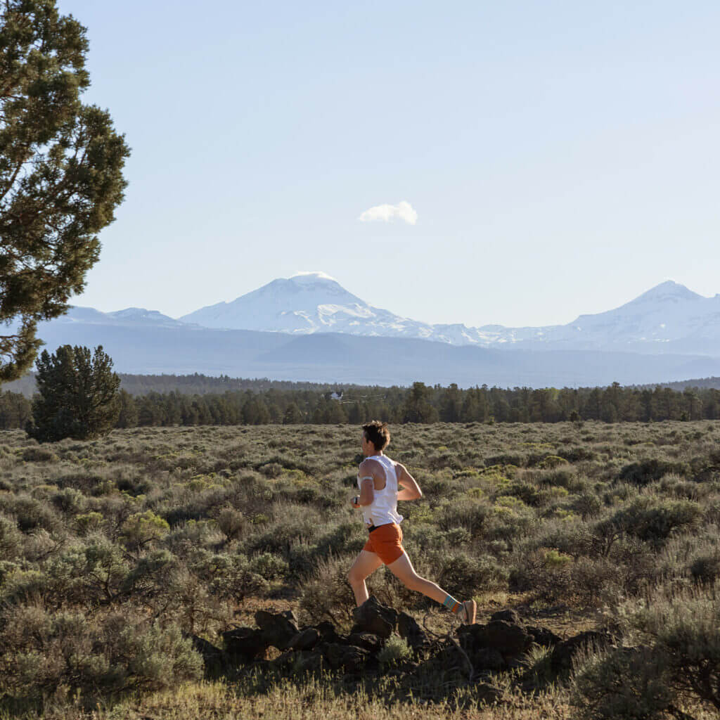 A person runs through a lush, open field with a majestic mountain range in the distance in Central Oregon.