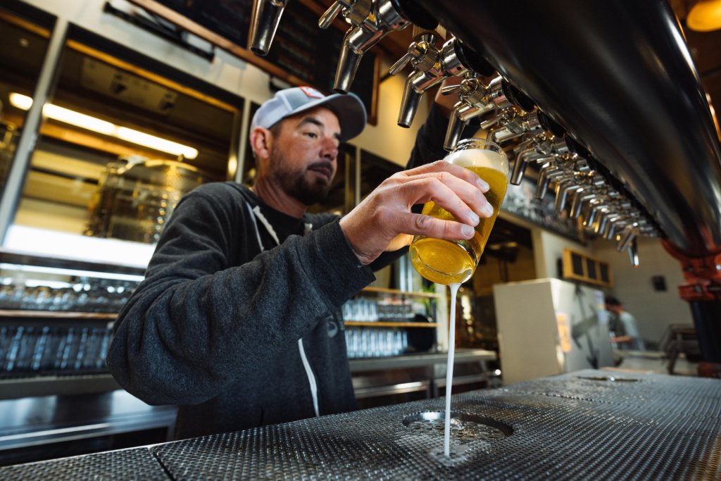 A bearded man pours a frothy beer from a tap into a glass at a bar in Central Oregon.