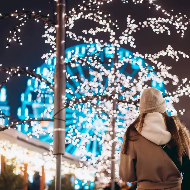 A woman in a beanie and coat admires a lit Ferris wheel at night in Central Oregon.