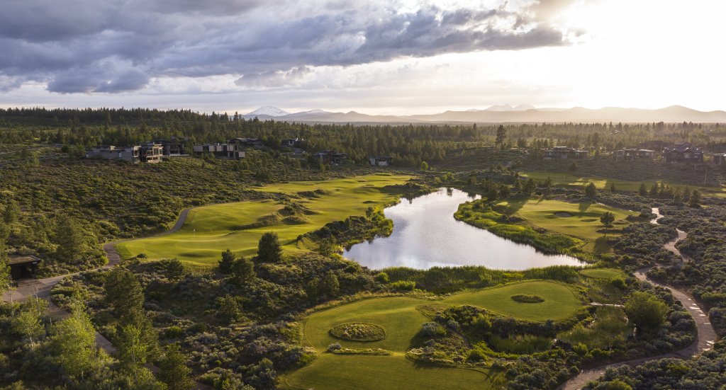 A serene landscape featuring a golf course with a winding river and distant mountains in Central Oregon.