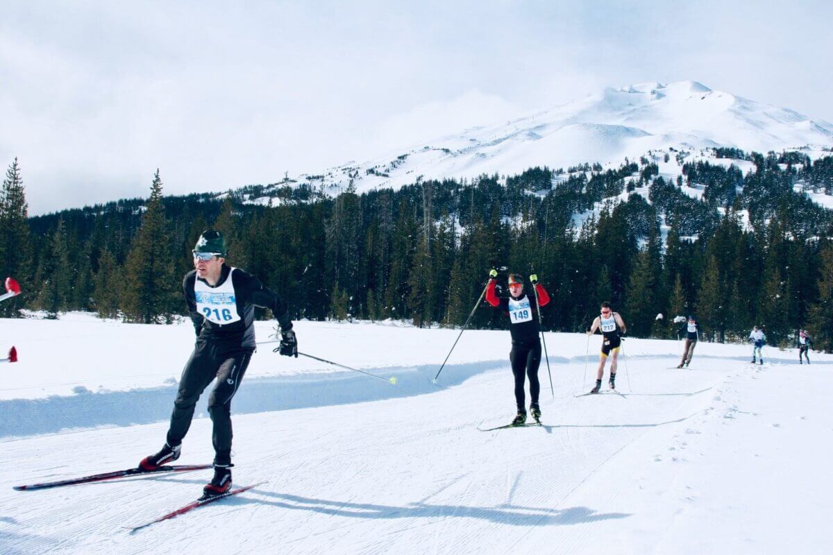 Cross-country skiers racing through a snowy forest with a mountain peak in the distance in Central Oregon.