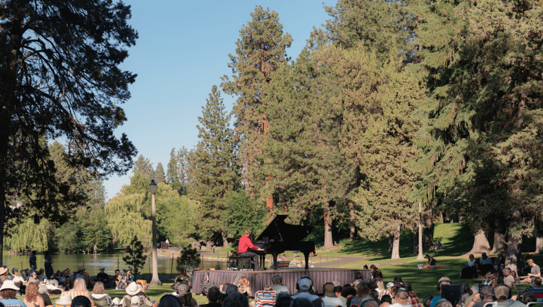 A vibrant outdoor concert featuring a pianist in a red shirt, surrounded by an audience in a lush park setting in Central Oregon.