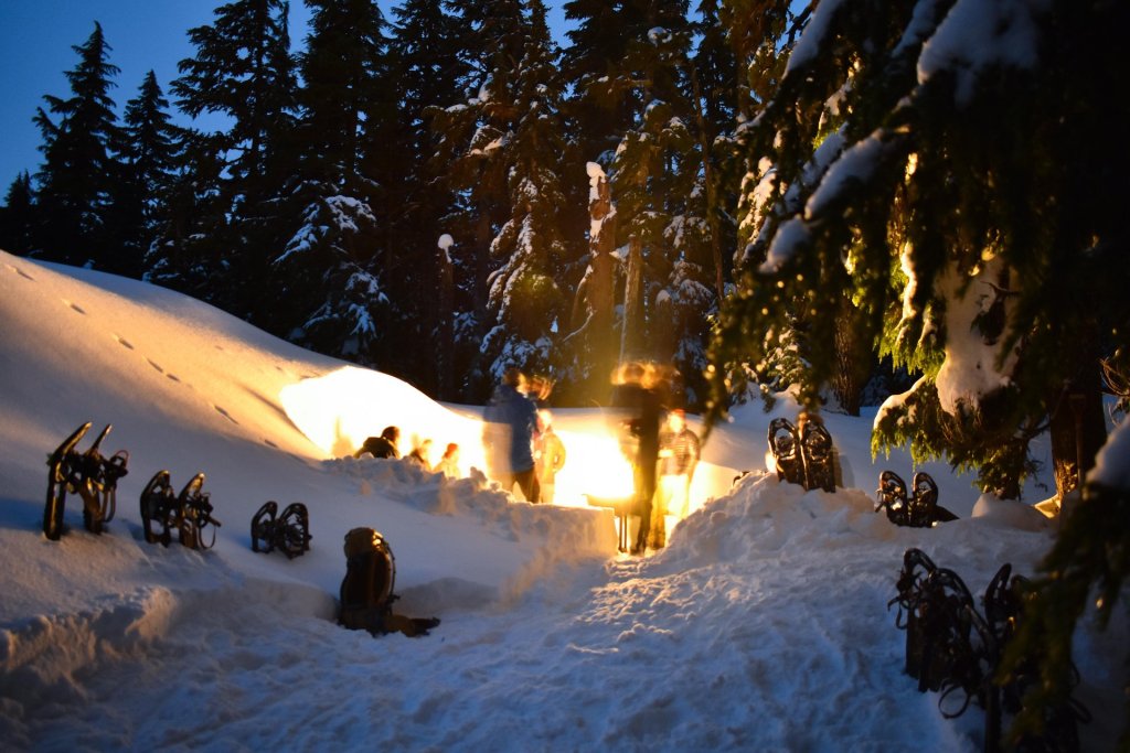 A group of people gathered around a campfire in a snowy forest at night in Central Oregon.