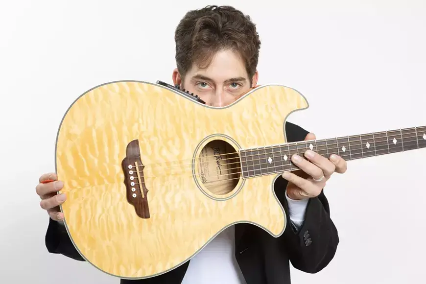 A musician holding a large acoustic guitar, showcasing its intricate design and craftsmanship in Central Oregon.