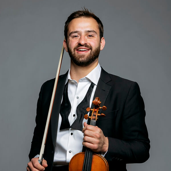 A smiling violinist in a tuxedo holds a violin and bow in Central Oregon.