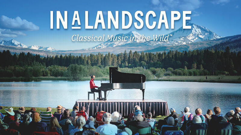 A pianist performs on a stage by a serene lake, surrounded by majestic mountains and a lush forest in Central Oregon.