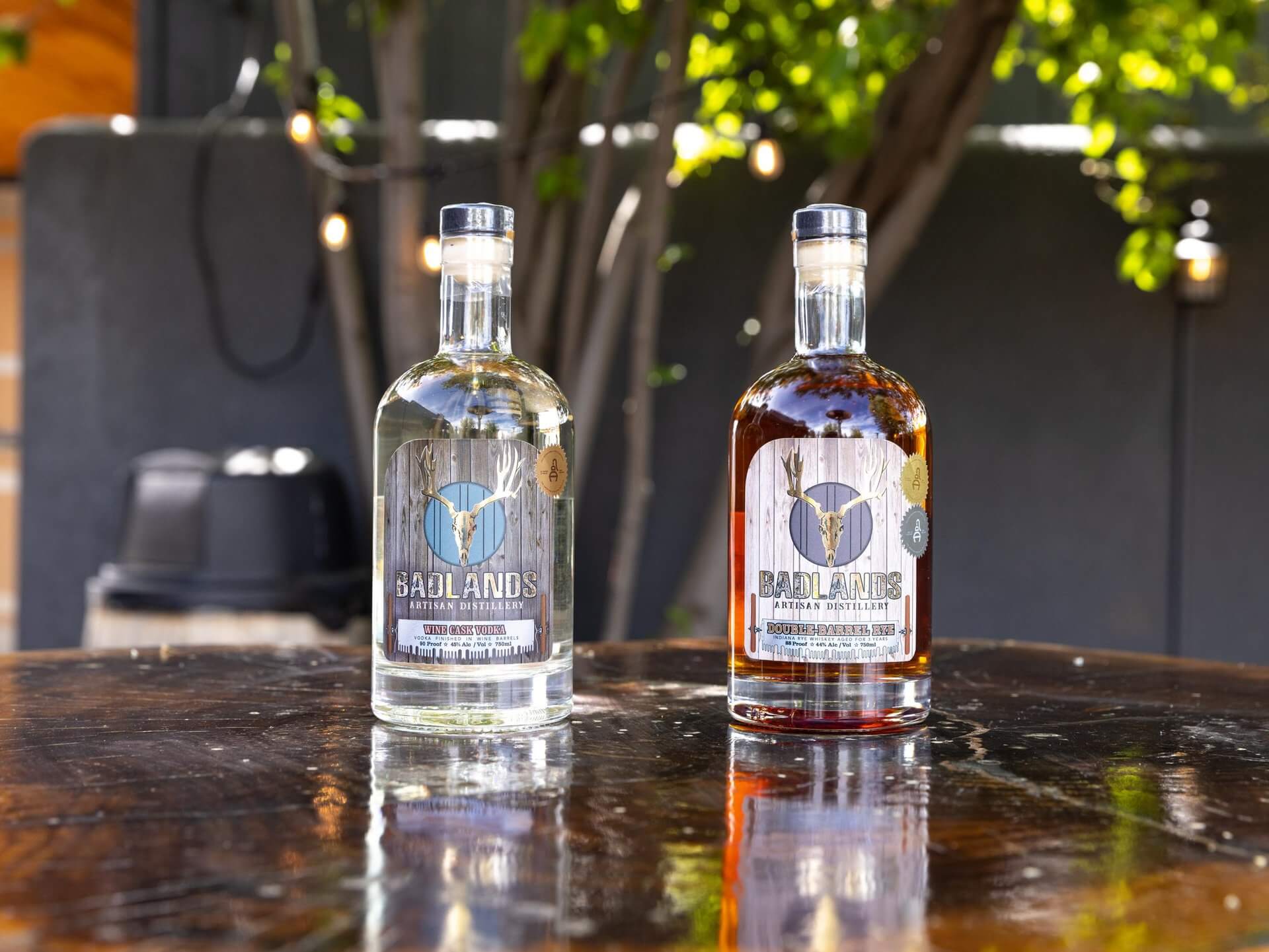 Two bottles of Badlands Distillery's Badlands Vodka, one clear and one amber, sit on a wooden table in Central Oregon.