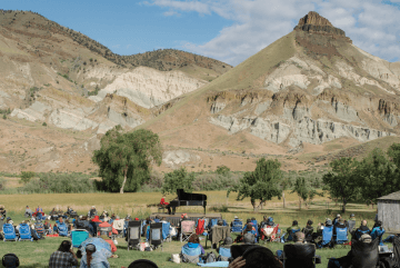 An outdoor concert featuring a grand piano on a stage set against a backdrop of rugged mountains in Central Oregon.