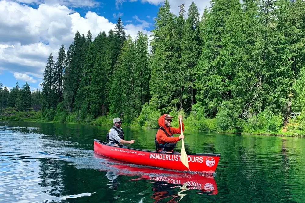 Two men in a red canoe paddling through a serene lake surrounded by dense forest in Central Oregon.