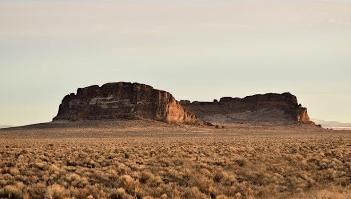 A vast desert landscape with rugged rock formations under a clear sky in Central Oregon.