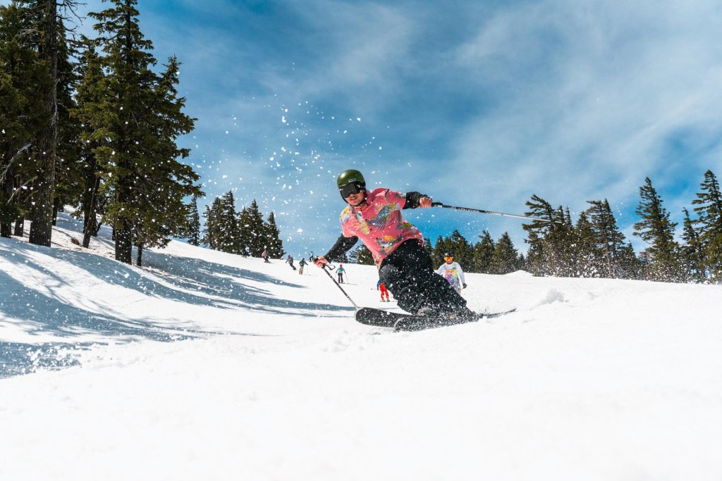 A skier in a pink and yellow outfit glides down a snowy slope, surrounded by tall trees in Central Oregon.
