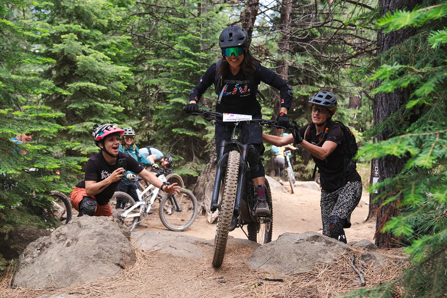 Mountain bikers navigate a challenging trail, surrounded by lush forest and supportive friends in Central Oregon.