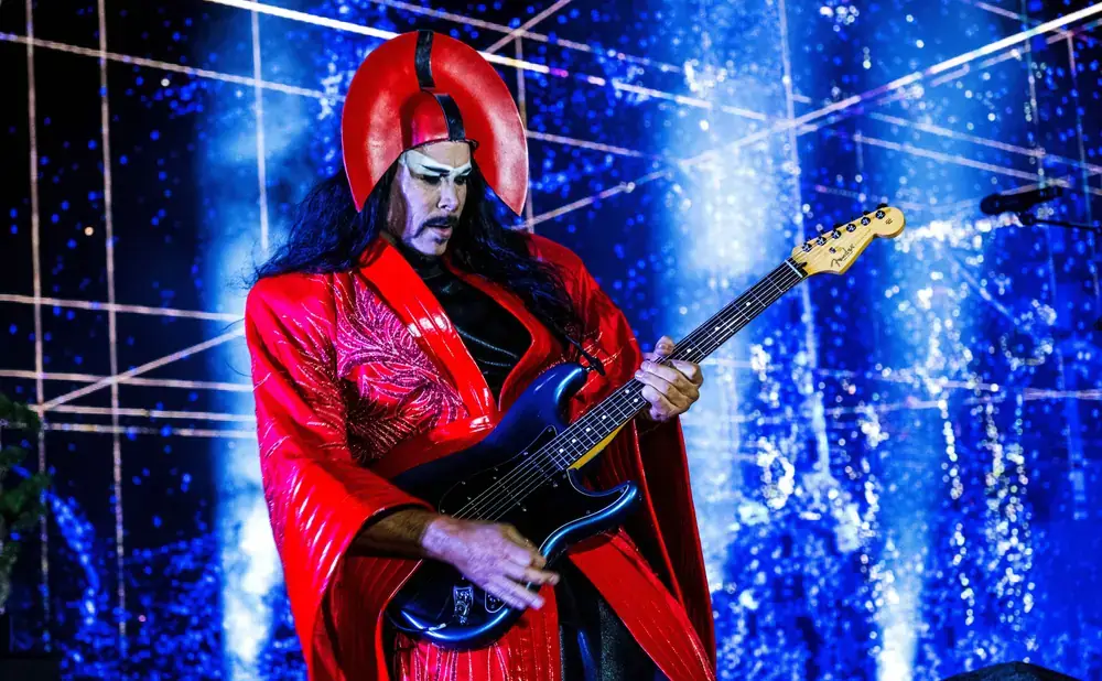 A musician in a red and gold outfit plays a guitar on stage with a cosmic backdrop in Central Oregon.