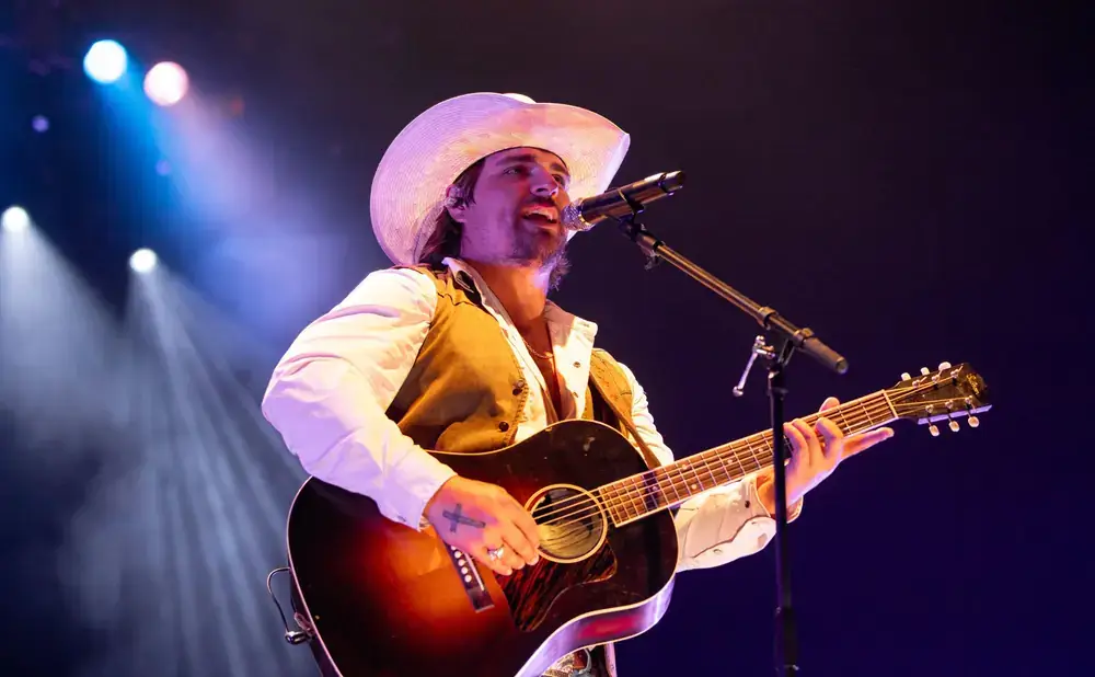 A musician in a cowboy hat performs on stage, strumming an acoustic guitar and singing into a microphone in Central Oregon.