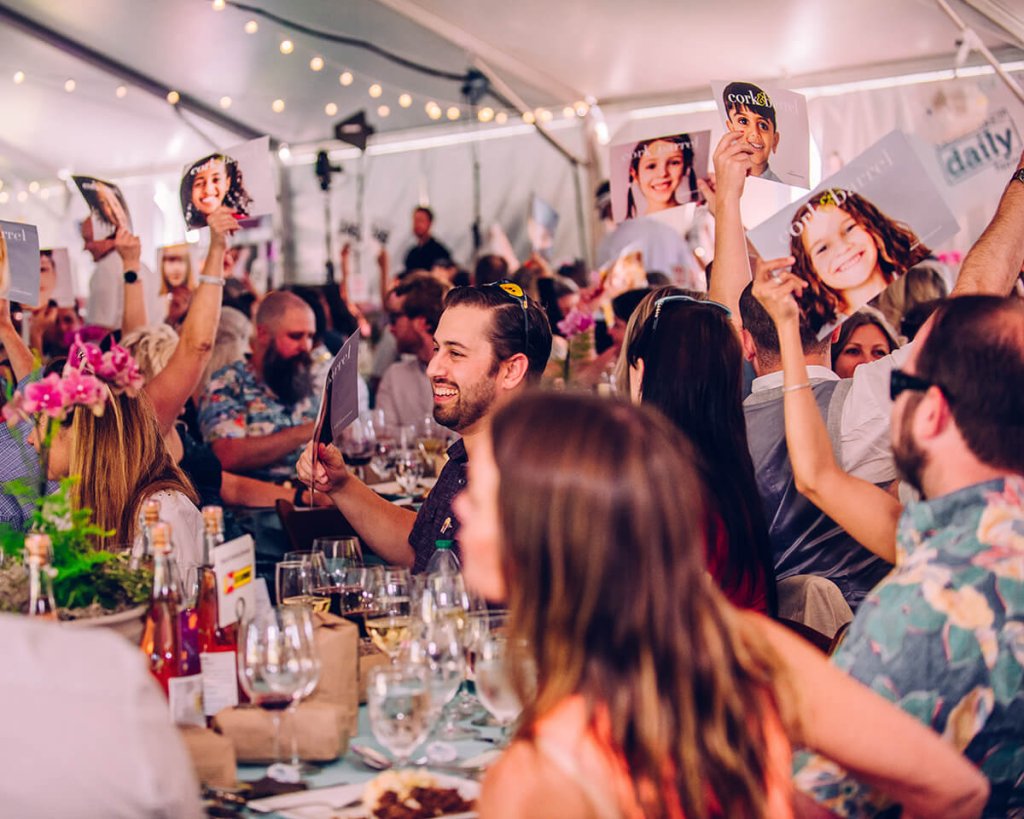 A lively gathering of people at a tented event, holding up photographs and smiling in Central Oregon.