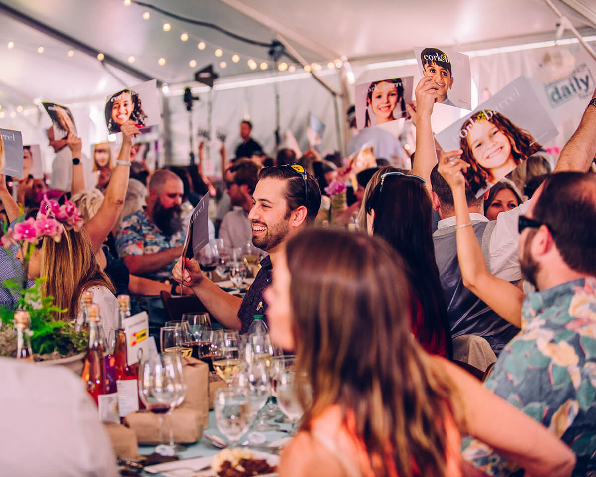 A lively gathering of people at a tented event, holding up photographs and smiling in Central Oregon.