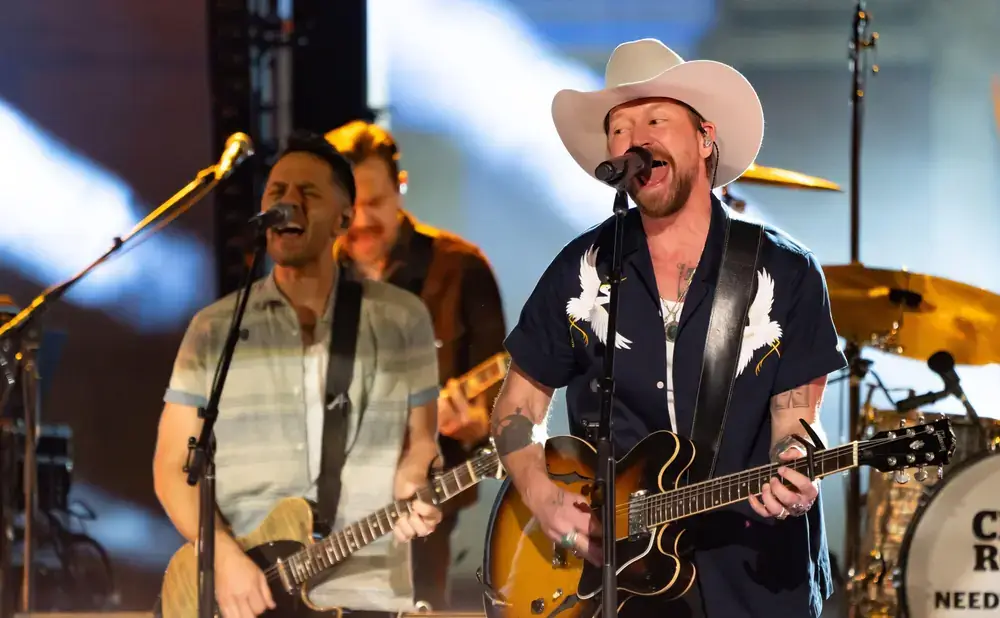 A musician in a cowboy hat performs with a band on stage, singing into a microphone while playing guitar in Central Oregon.