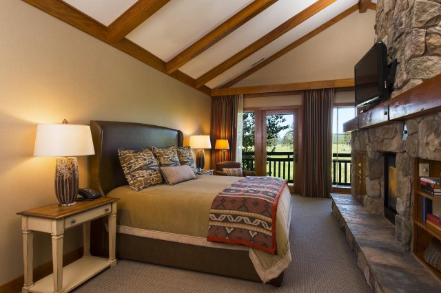 A cozy mountain lodge bedroom with a fireplace, stone walls, and a view of rolling hills in Central Oregon.