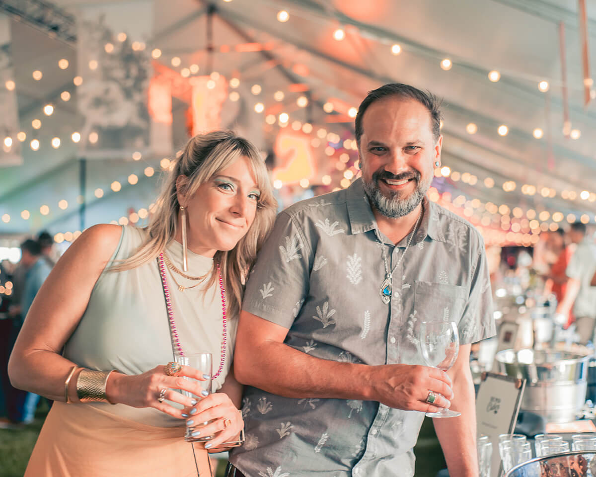 A couple at a festive event, smiling and drinking, surrounded by string lights and a lively atmosphere in Central Oregon.