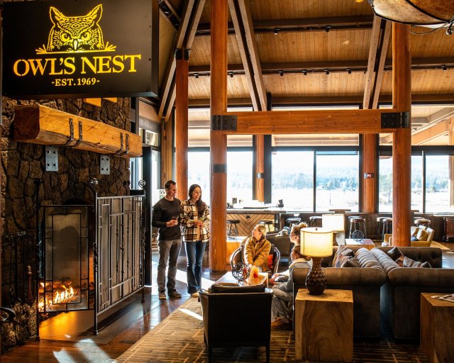 A cozy interior of a rustic cabin with a fireplace and large windows overlooking a snowy landscape in Central Oregon.