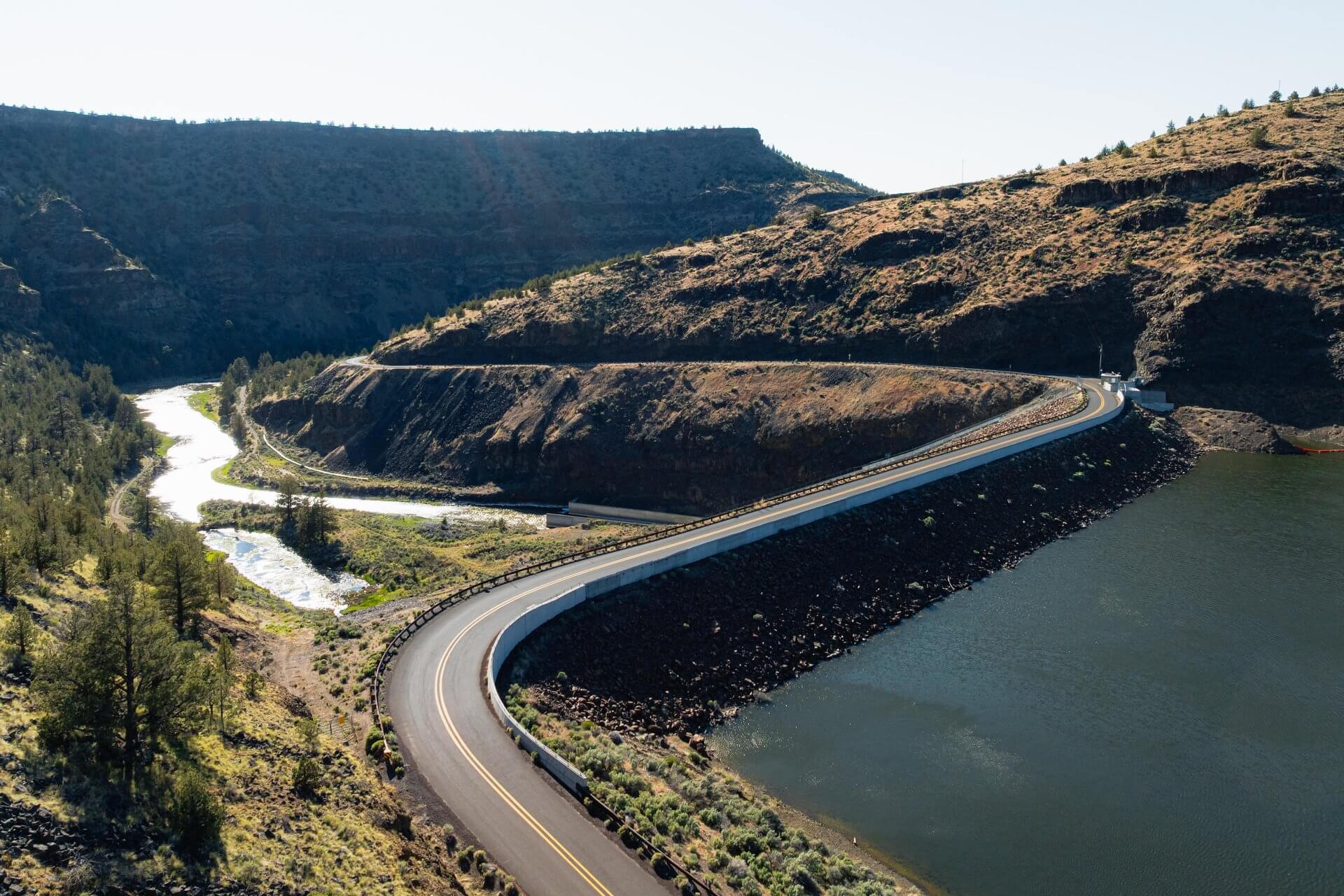 A winding road alongside a river in a mountainous landscape in Central Oregon.