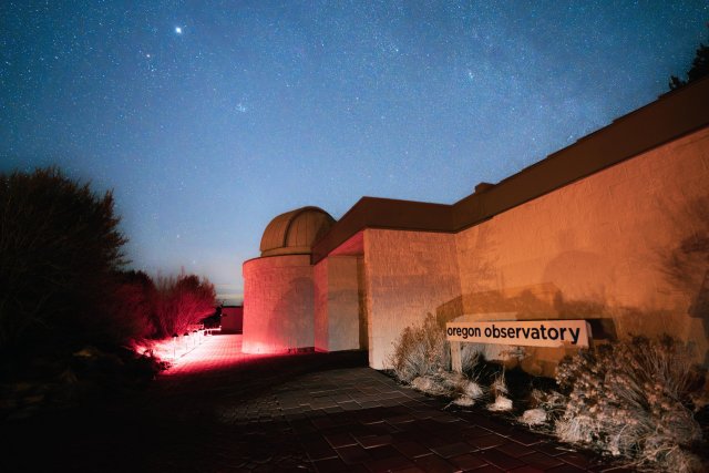 Oregon Observatory at night, illuminated by red and blue lights, with stars in the sky in Central Oregon.