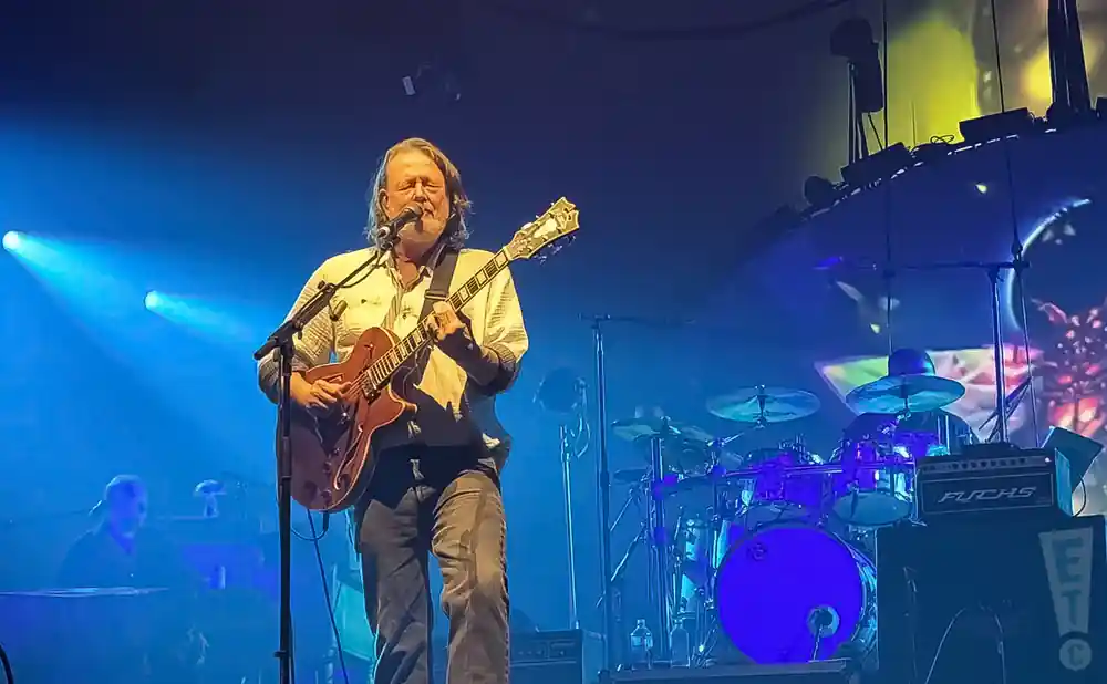 A musician performs on stage with a guitar and microphone, surrounded by a vibrant light show in Central Oregon.
