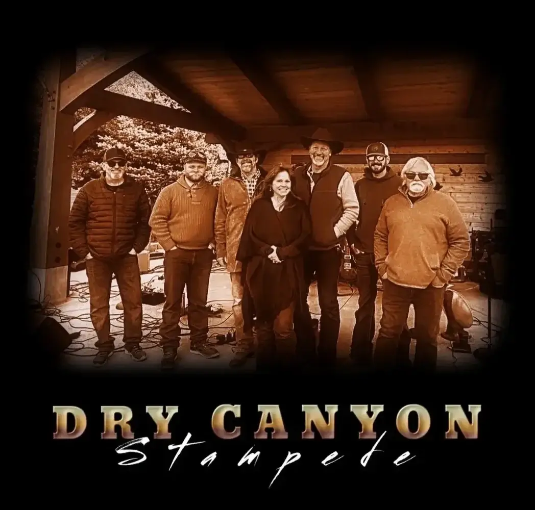A group of six people, including four men and two women, stand together under a wooden shelter, smiling and posing for a photo in Central Oregon.