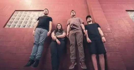Four individuals lean against a red brick wall, appearing weightless and relaxed in Central Oregon.
