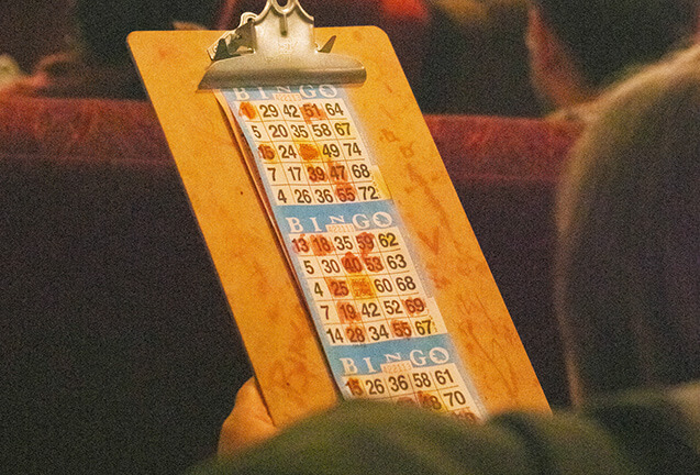 A person holding a wooden clipboard with a bingo card attached, featuring marked numbers in Central Oregon.