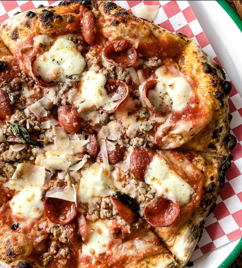 A mouthwatering pizza with a charred crust, topped with pepperoni, sausage, melted mozzarella, and shaved Parmesan cheese in Central Oregon.