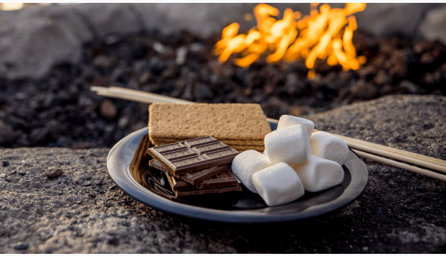 A plate of s'mores ingredients, including graham crackers, chocolate bars, and marshmallows, with a crackling fire in the background in Central Oregon.