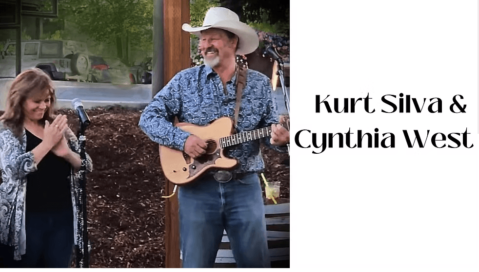 A man in a cowboy hat plays guitar while a woman claps beside him at an outdoor event in Central Oregon.