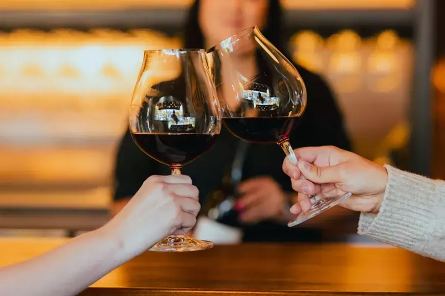 Two hands clinking wine glasses filled with red wine on a wooden bar counter in Central Oregon.