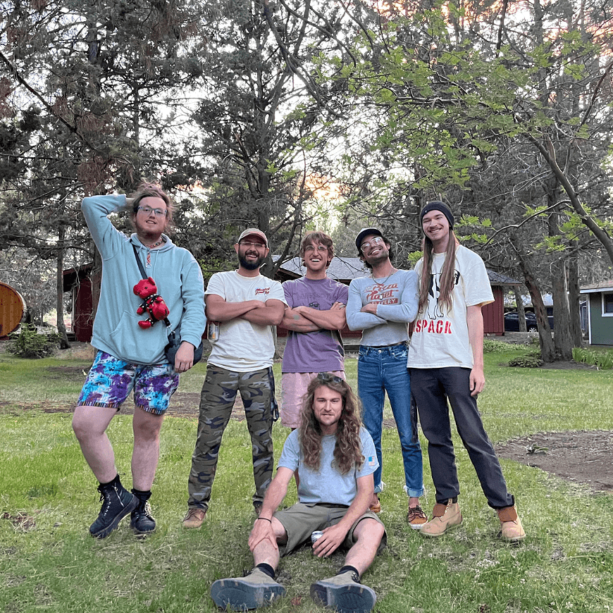 A group of six friends posing together in a grassy area surrounded by trees at sunset in Central Oregon.