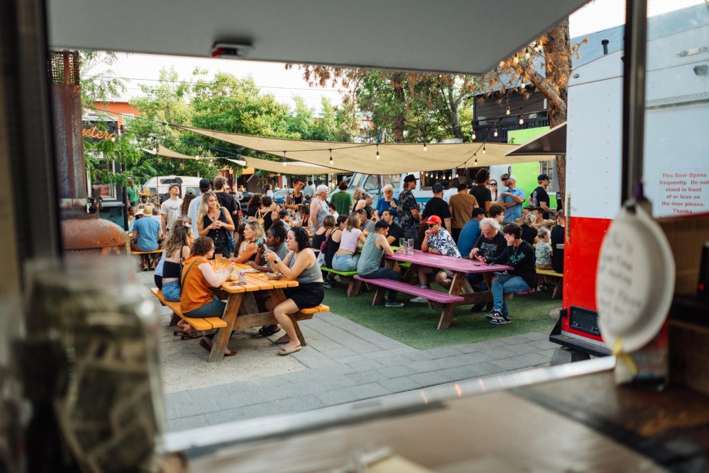A bustling outdoor food truck event with people enjoying meals at colorful picnic tables under string lights in Central Oregon.