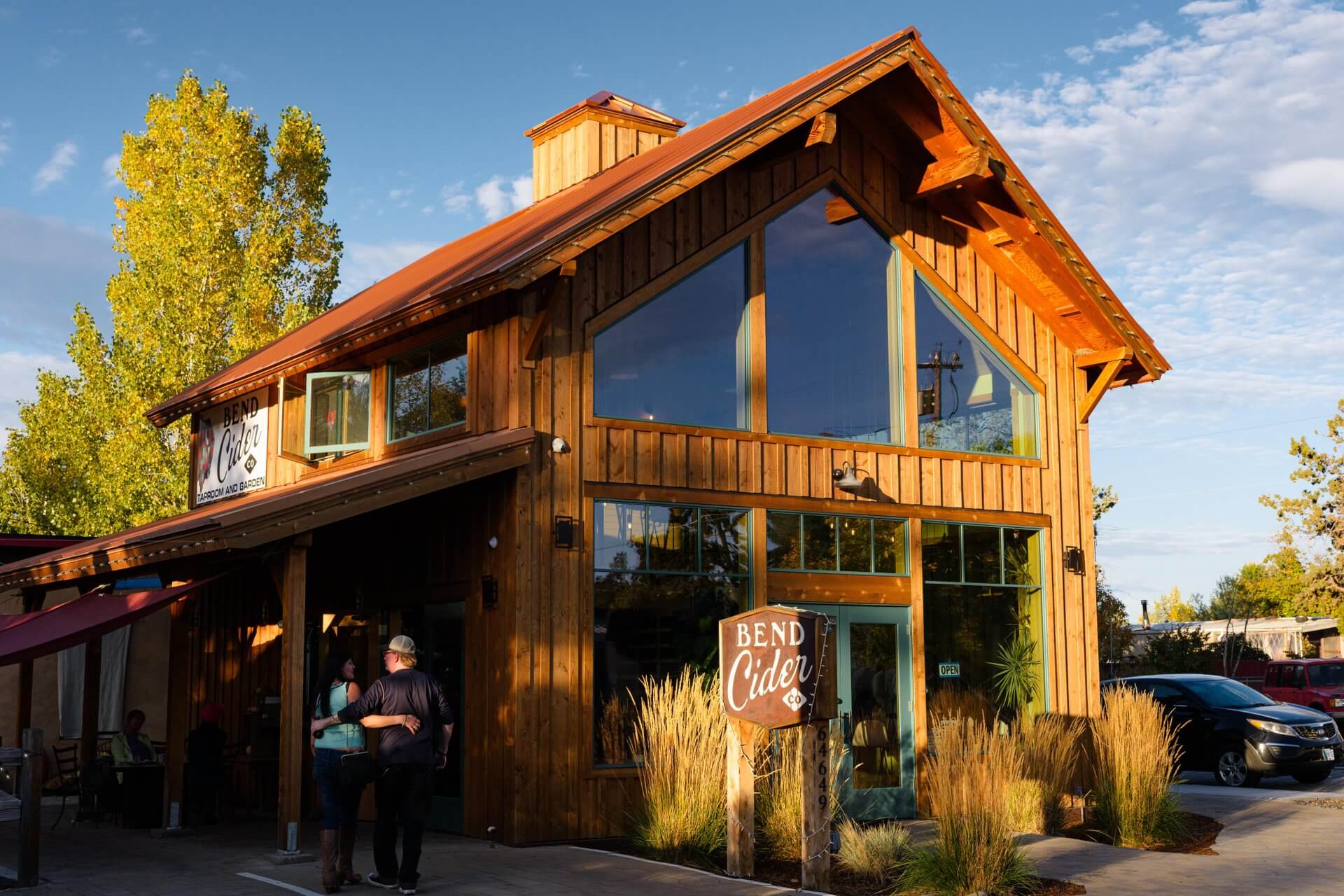 A rustic wooden building with a red roof and large windows, surrounded by trees and a sign reading 'Bend Cider' in Central Oregon.