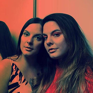 Two women with long hair, one in a black and white dress, the other in red, standing close together in Central Oregon.