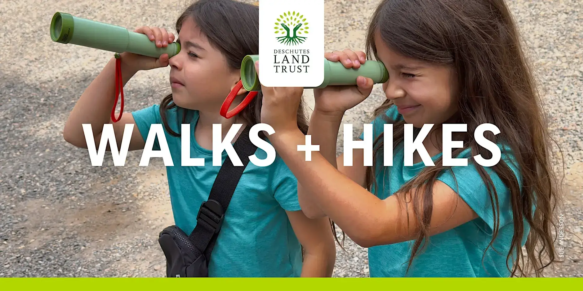 Two young girls, dressed in matching blue shirts, are exploring the outdoors together, using green toy telescopes to look at the sky and trees in Central Oregon.