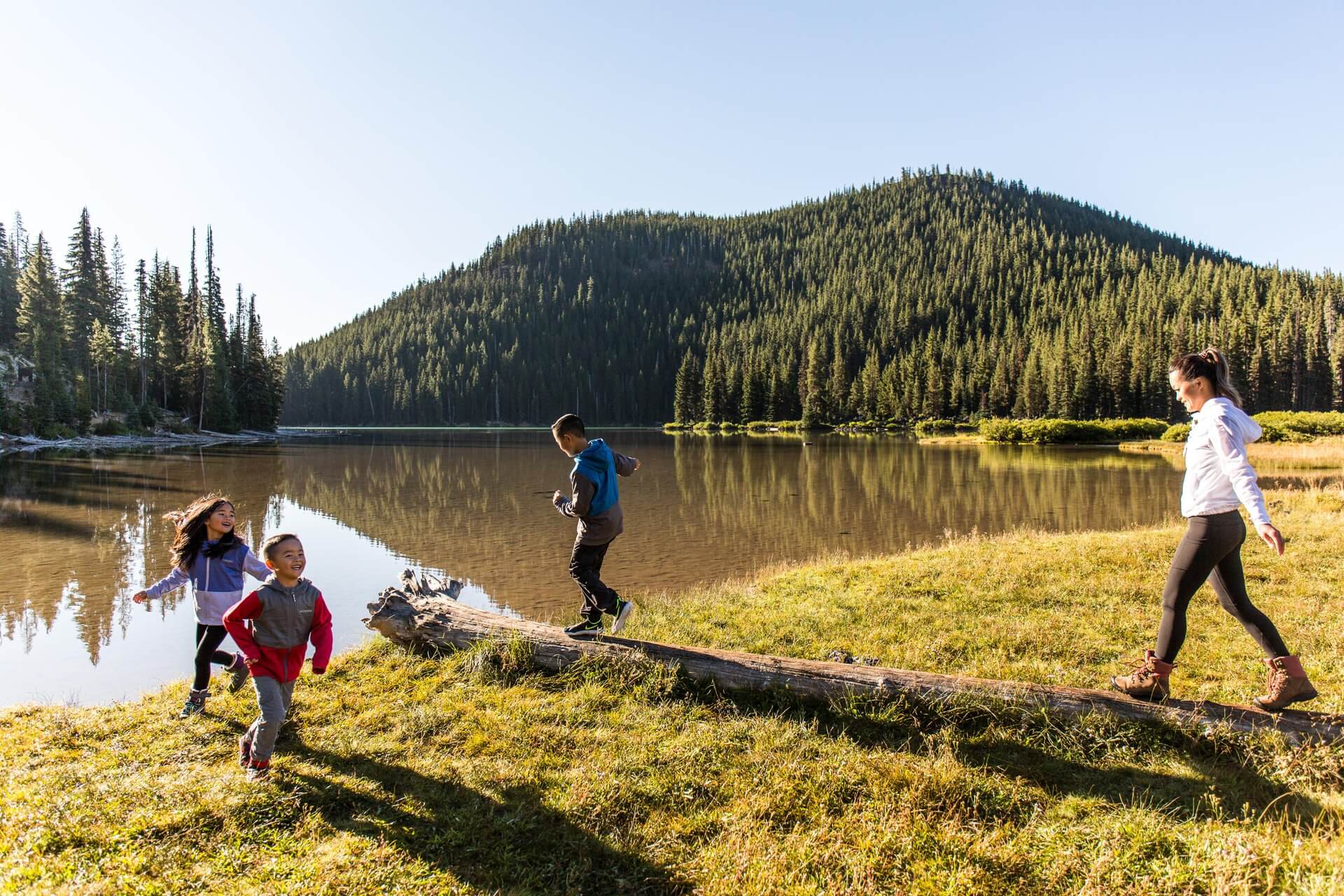 A family enjoys a sunny day hiking near a serene mountain lake surrounded by tall evergreen trees in Central Oregon.
