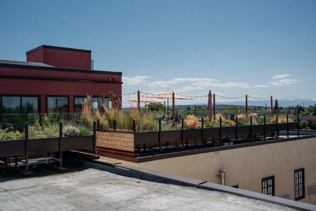 A rooftop garden with wooden planters and string lights, overlooking a cityscape and distant mountains in Central Oregon.