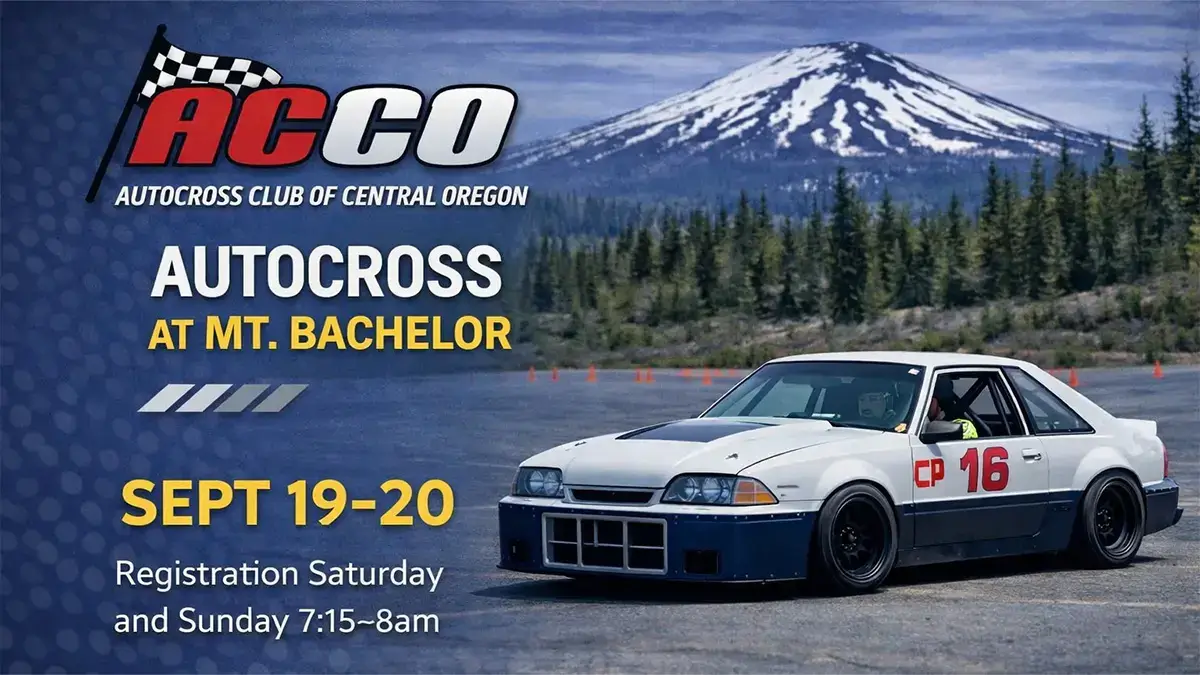 A white race car with the number 16 on its side is parked on a paved surface, with a backdrop of a snow-capped mountain and a forest of evergreen trees in Central Oregon.