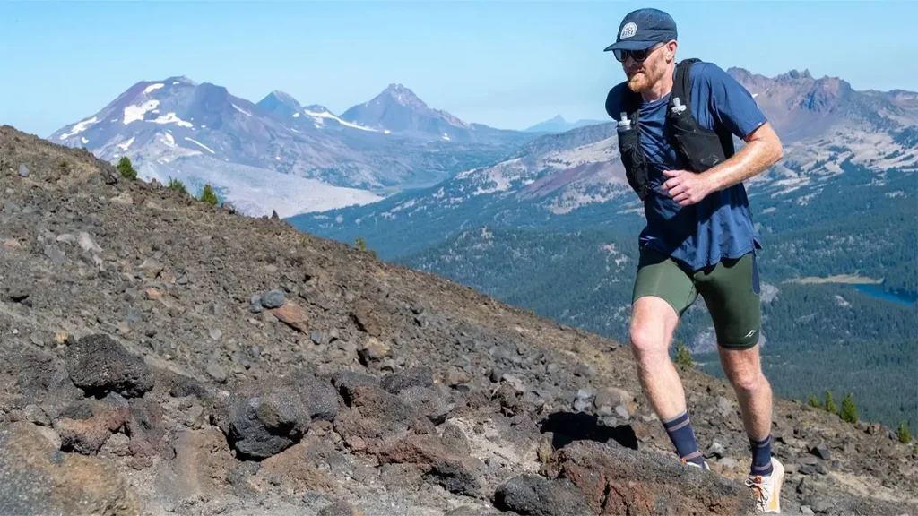 A hiker ascends a rocky volcanic slope with snow-capped mountains in the distance in Central Oregon.