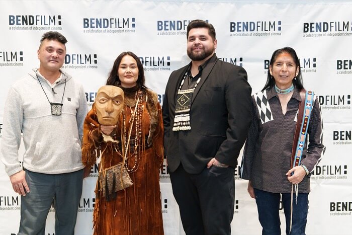 Four individuals pose together at a BendFilm event, showcasing diverse attire and accessories in Central Oregon.