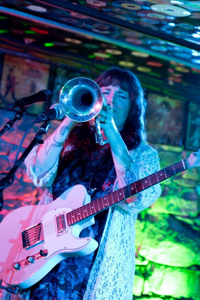 A musician passionately plays a trumpet and guitar in a vibrant, colorful venue in Central Oregon.