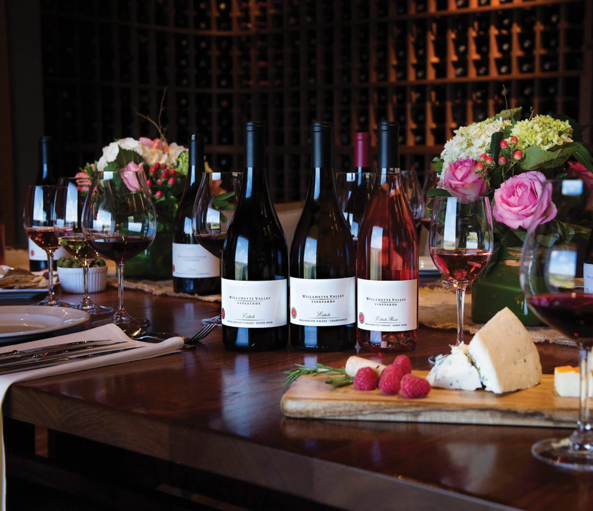 A wine tasting setup with various bottles, glasses, and a cheese board on a wooden table in Central Oregon.