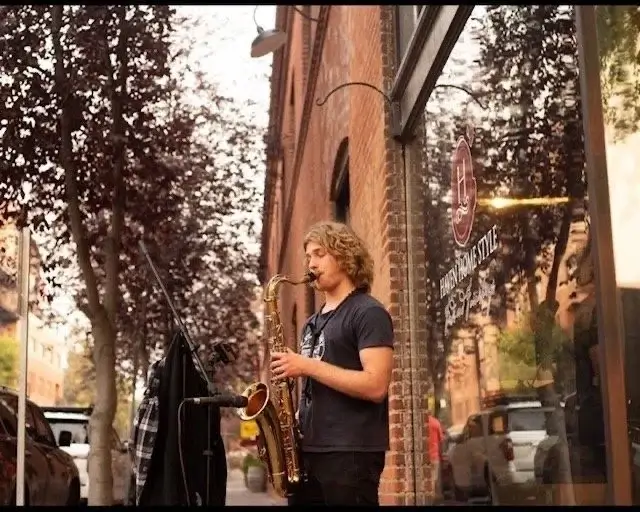 A young musician plays the saxophone on a city street corner, surrounded by autumn foliage in Central Oregon.